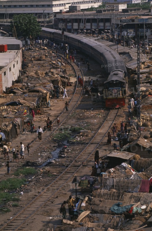 BANGLADESH, Dhaka, Train travelling through Tejgoan slum with ramshackle dwellings beside tracks and people living amongst rubbish and polluted water.