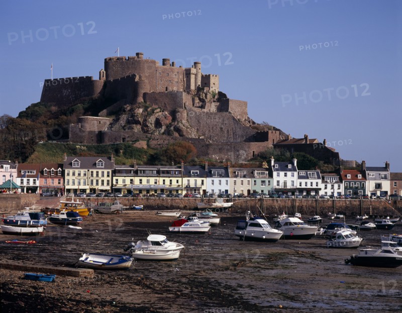 UNITED KINGDOM, Channel Islands, Jersey, Grouville. Gorey Castle or Mont Orgueil set on hill overlooking village buildings and boats in harbour with the tide out. On the east coast.