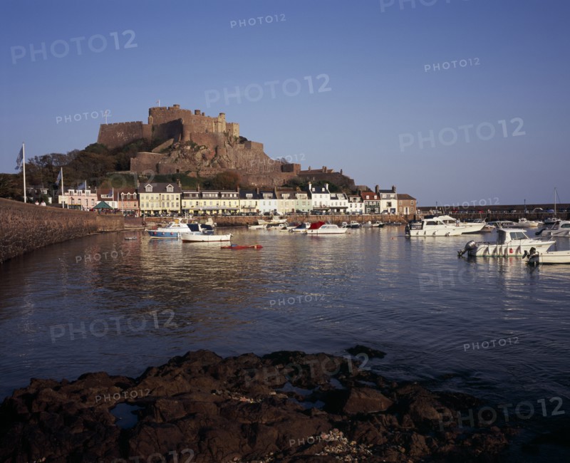 UNITED KINGDOM, Channel Islands, Jersey, Grouville. Gorey Castle or Mont Orgueil set on hill overlooking village buildings and boats in harbour with the tide in. On the east coast.