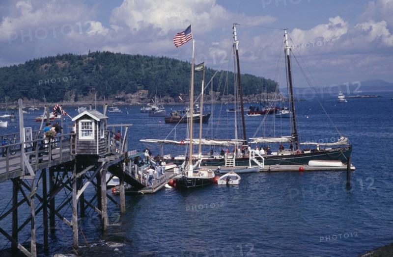 USA, Maine, Bar Harbour, "Wooden jetty with yacht moored at side, various boats on water and tree covered headland beyond."