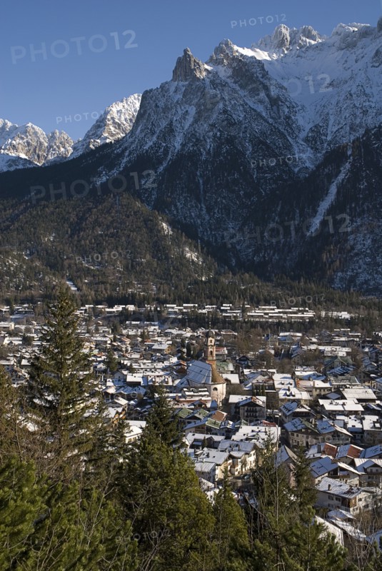 GERMANY, Bavaria, Mittenwald, View over Mittenwald town rooftops from surrounding hillside with snow covered mountains behind