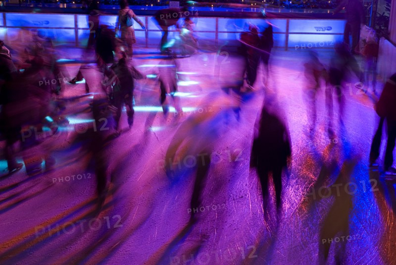 GERMANY, Bavaria, Munich, Ice Skaters in motion blur with multi coloured light on a winter ice rink in the city centre