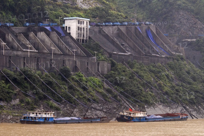 CHINA, Hubei , Sandouping, Industrial complex in the Wu Gorge. Line of trucks bring coal from the mines and dump into bunkers from where it flows through pipes to coal barges waiting below on the Yangtze River