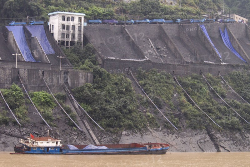CHINA, Hubei , Sandouping, Industrial complex in the Wu Gorge. Line of trucks bring coal from the mines and dump into bunkers from where it flows through pipes to coal barges waiting below on the Yangtze River