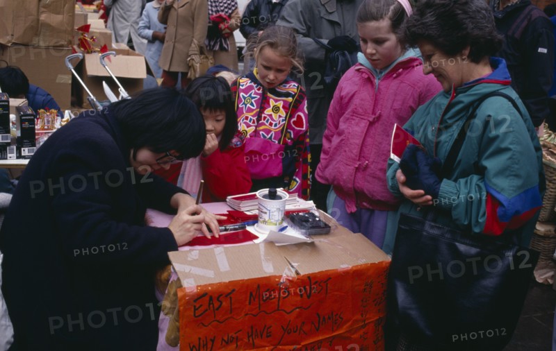 ENGLAND, London, Chinese New Year, Calligraphist writing Western names in Chinese during New Year celebrations in Chinatown.  Sign beside stall reads ‘East Meets West’.