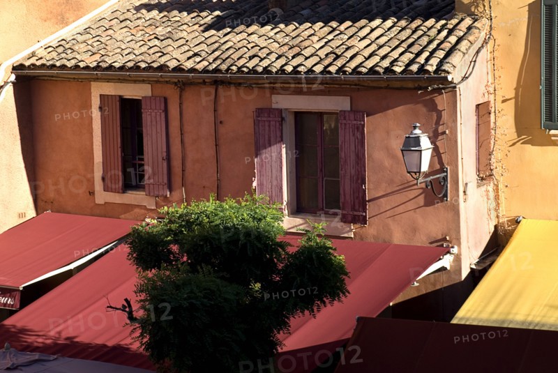 FRANCE, Provence Cote d’Azur, Vaucluse, "Roussillon.  Provencal colours in the town centre, exterior facade of building with tiled roof, red awning and pale ochre and orange walls."