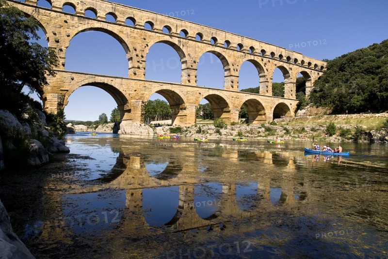 FRANCE, Provence Cote d’Azur, Gard, Pont du Gard.  View from west side of the Roman aqueduct in glowing evening light with passing canoes and reflection in water below.