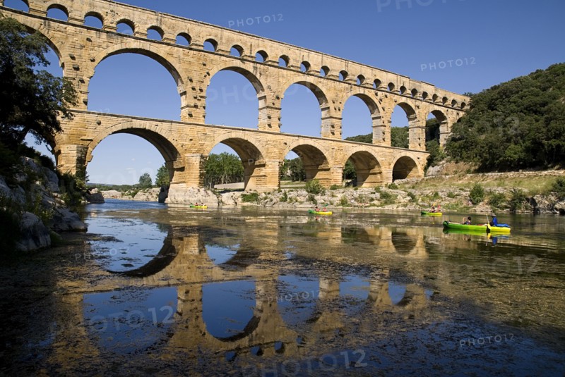 FRANCE, Provence Cote d’Azur, Gard, Pont du Gard.  View from west side of the Roman aqueduct in glowing evening light with passing canoes and reflection in the water below.