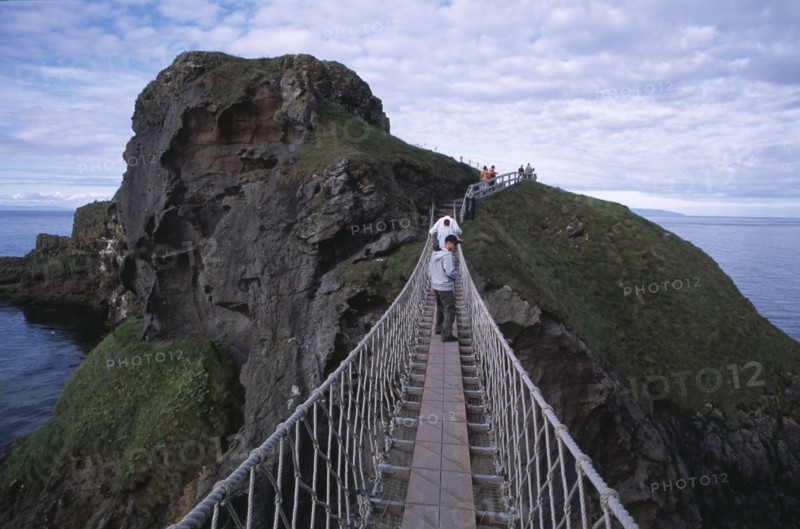 NORTHERN IRELAND, County Antrim, Ballintoy, Carrick-a-Rede Rope Bridge. Vistors walking over rope bridge linking a rocky island to cliffs.