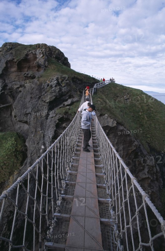 NORTHERN IRELAND, County Antrim, Ballintoy, Carrick-a-Rede Rope Bridge. Vistors walking over rope bridge linking a rocky island to cliffs.