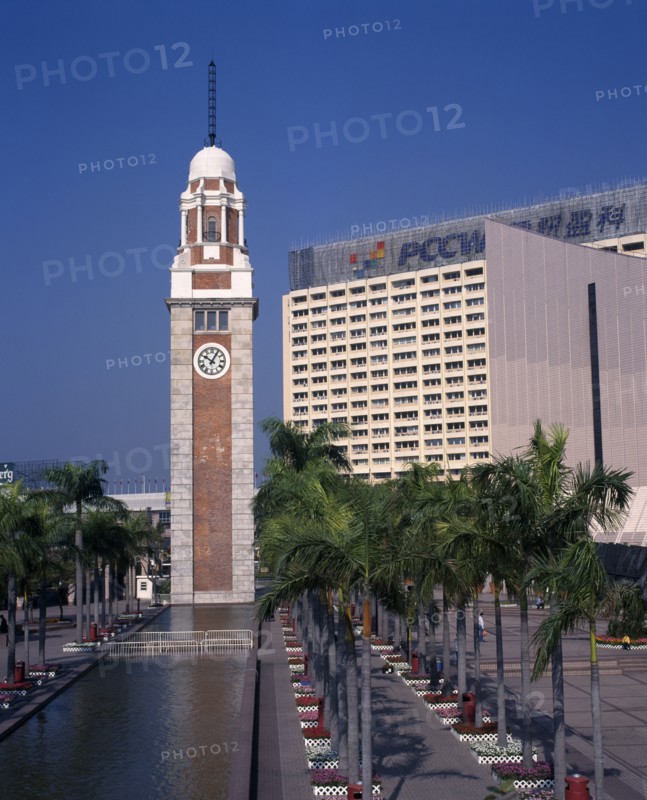 CHINA, Hong Kong, Kowloon, Kowloon Star ferry clock tower at end of rectangular pool lined by palms and flowerbeds.