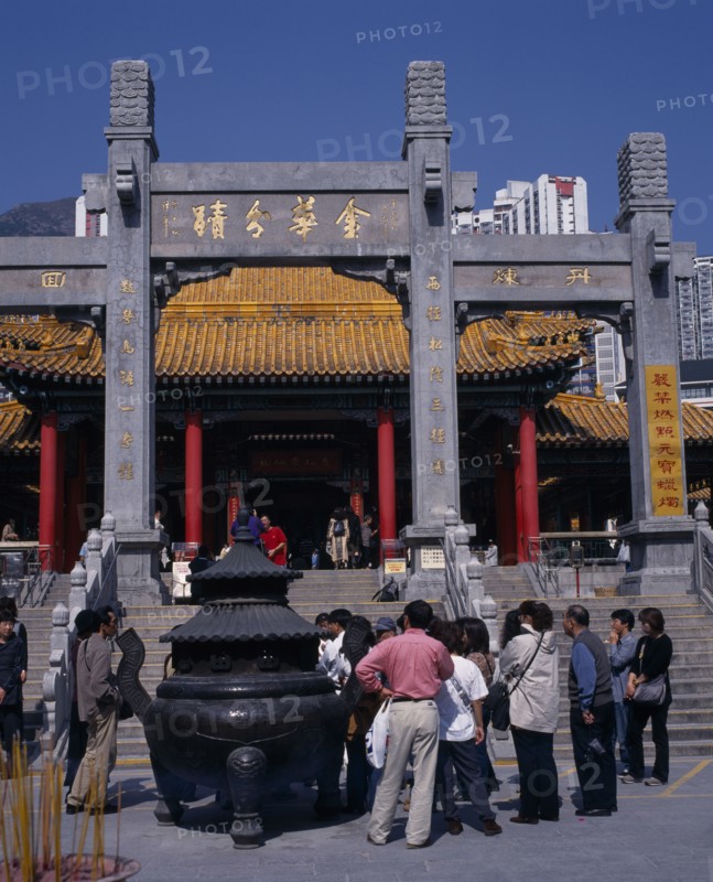 CHINA, Hong Kong, Kowloon, Wong Tai Sin taoist temple established in 1921.  Visitors gathered beside incense burner at foot of flight of steps to entrance built in traditional Chinese style with red interior pillars and pagoda style roof.