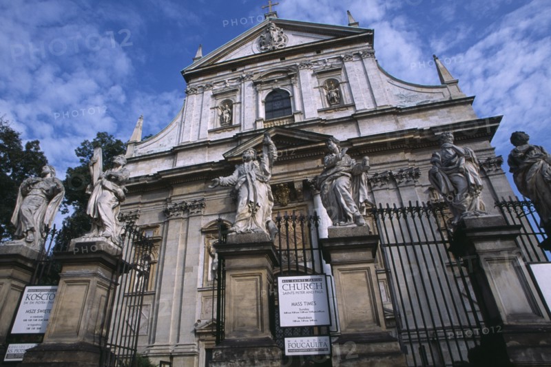 POLAND, Krakow, Exterior facade of Church of Saints Peter and Paul with  statues of the twelve disciples and religious iconography and sign detailing times of Mass services on ironwork gate.