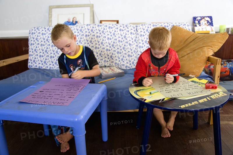 RELIGION, Festivals, Christmas, Two young left handed boys on Christmas Eve sitting down on a sofa and writing their Santa Lists at tables