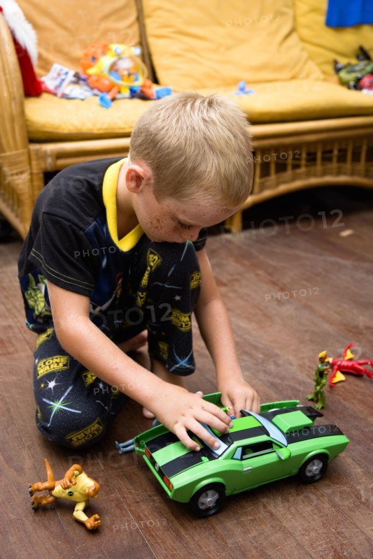 RELIGION, Festivals, Christmas, Young boy in his pyjamas playing on the floor with his green toy car and other presents on Christmas Day