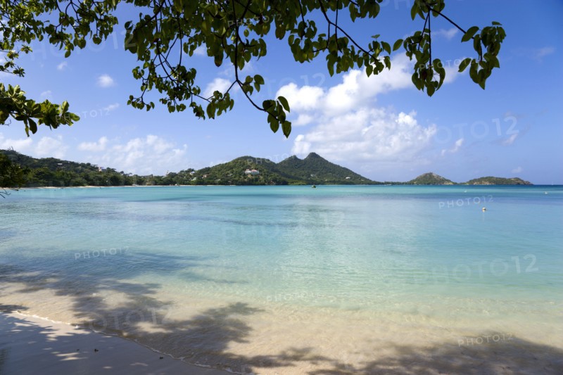 WEST INDIES, Grenada, Carriacou, The calm clear blue water breaking on Paradise Beach in L'Esterre Bay with Point Cistern and The Sister Rocks in the distance