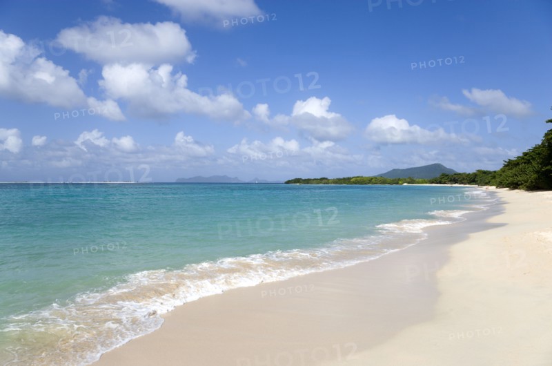 WEST INDIES, Grenada, Carriacou, "The calm clear blue water breaking on Paradise Beach in L'Esterre Bay with Sandy Island, Petite Martinique and High North mountain in the distance and people walking along the sandy shore"