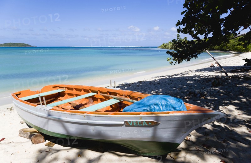 WEST INDIES, Grenada, Carriacou, The calm clear blue water breaking on Paradise Beach in L'Esterre Bay with Mabouya Island and Sandy Island in the distance. A small fishing boat sits on the beach out of the water