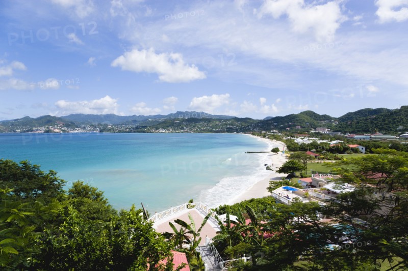 WEST INDIES, Grenada, St George, Gentle waves of the aquamarine sea breaking on the two mile stretch of the white sand Grand Anse Beach with the capital city of St George's in the distance