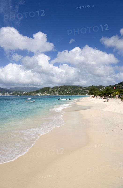 WEST INDIES, Grenada, St George, Waves of the aquamarine sea breaking on the two mile stretch of Grand Anse Beach with people on the white sandy beach and the capital city of St George's in the distance