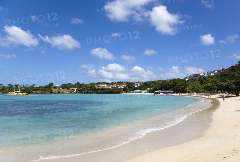 WEST INDIES, Grenada, St George, The aquamarine sea and tree lined white sand of BBC Beach in Morne Rouge Bay with tourists walking on the beach and tour boats moored