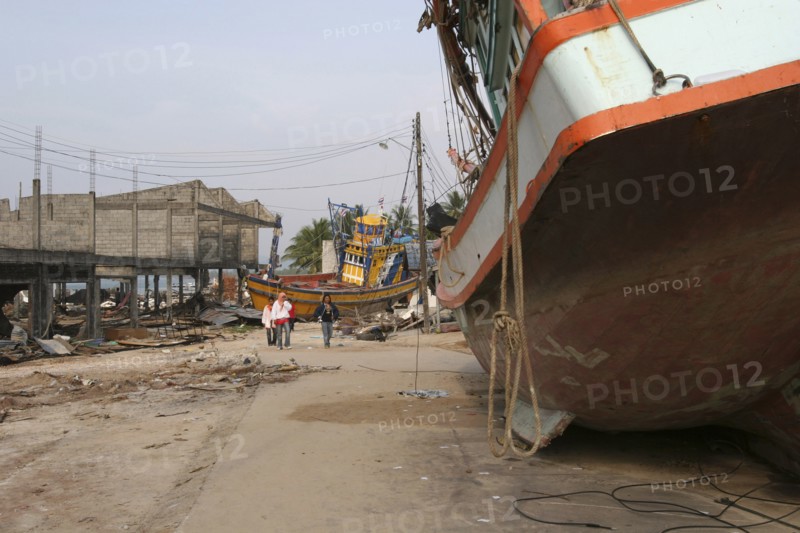 THAILAND, Phang Nga District, Nam Khem, "Tsunami. People walk past boats that have been pushed onto the streets in the village, nothing is left standing in the village 2500 people are pressumed dead 125kms north of Phuket on the 2nd Jan"