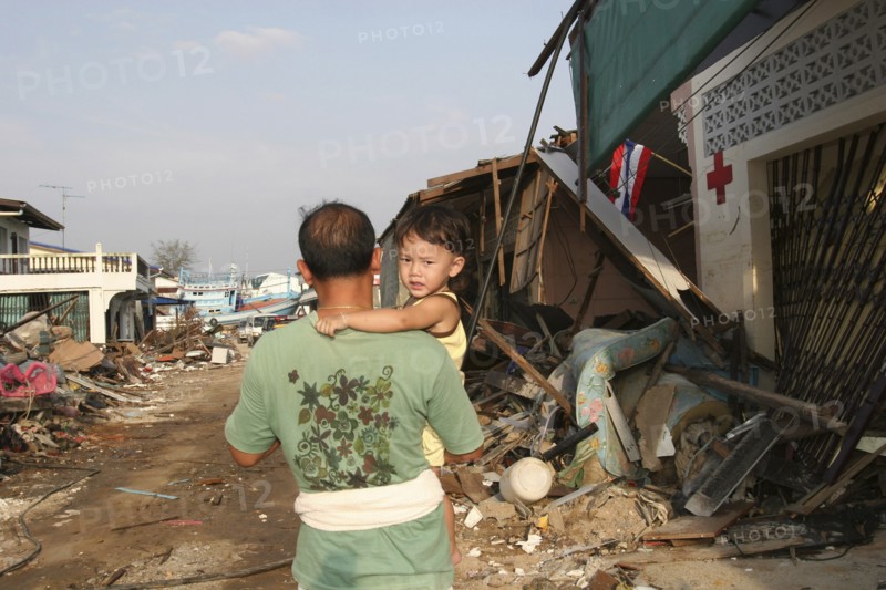 THAILAND, Phang Nga District, Nam Khem, Tsunami. One of the villagers with his child walks passed the remains of of his village after the damaged caused by the tsunami.Nothing is left standing in the village 2500 people are pressumed dead. 125kms north of Phuket on the 2nd Jan.