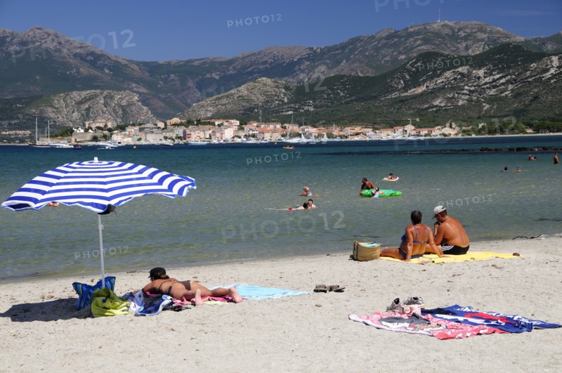 FRANCE, Corsica, St Florent, Bathers & sandy beach with St Florent old town in distance