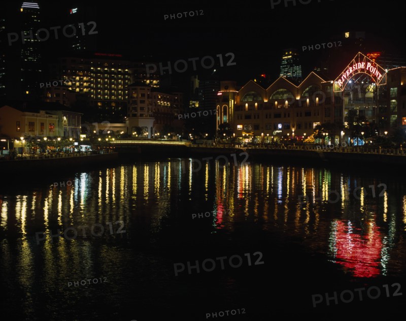 SINGAPORE, Cityscapes, Clarke Quay on the Singapore River. Waterside shops and restaurants illuminated at night with multi coloured lights reflected on the water