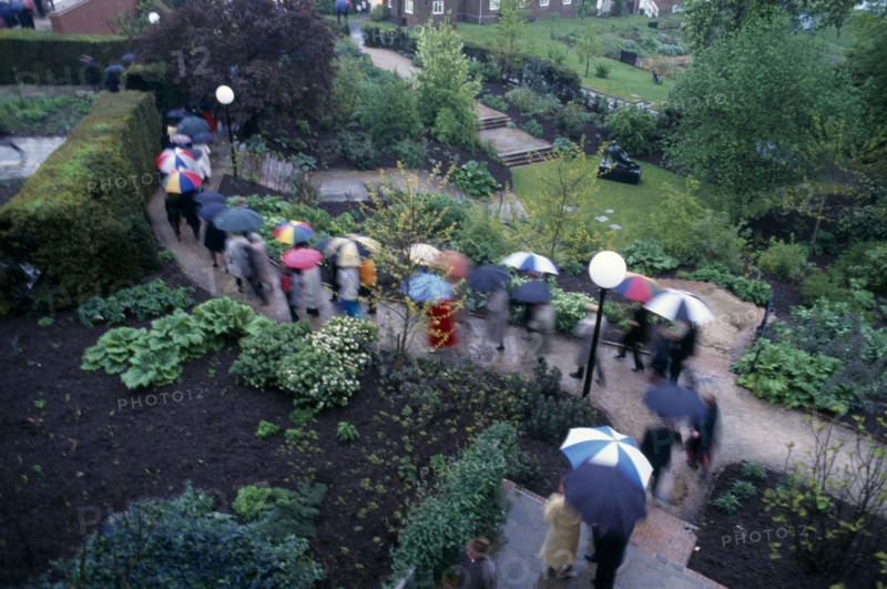 ENGLAND, East Sussex, Glyndebourne, Opera attendees walking through the gardens holding umbrellas in the rain.