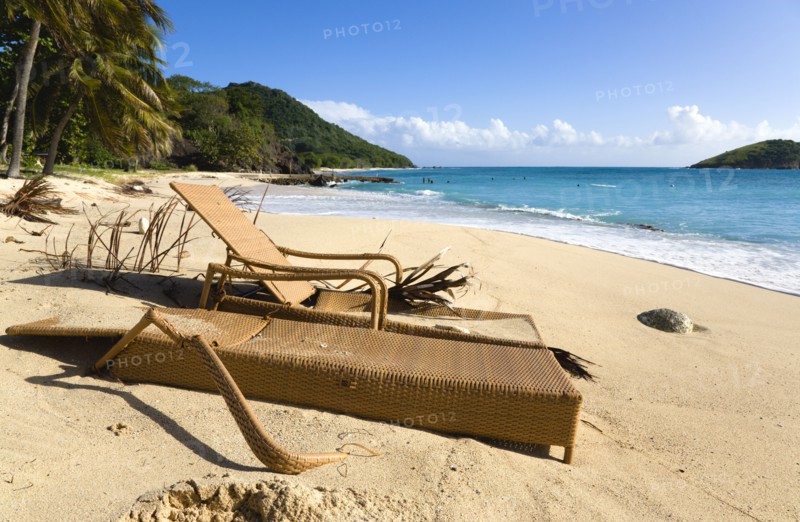 WEST INDIES, St Vincent & The Grenadines, Canouan, South Glossy Beach in Glossy bay with two damaged wooden sunbeds in the sand and waves from the turqoise sea breaking on the shore.