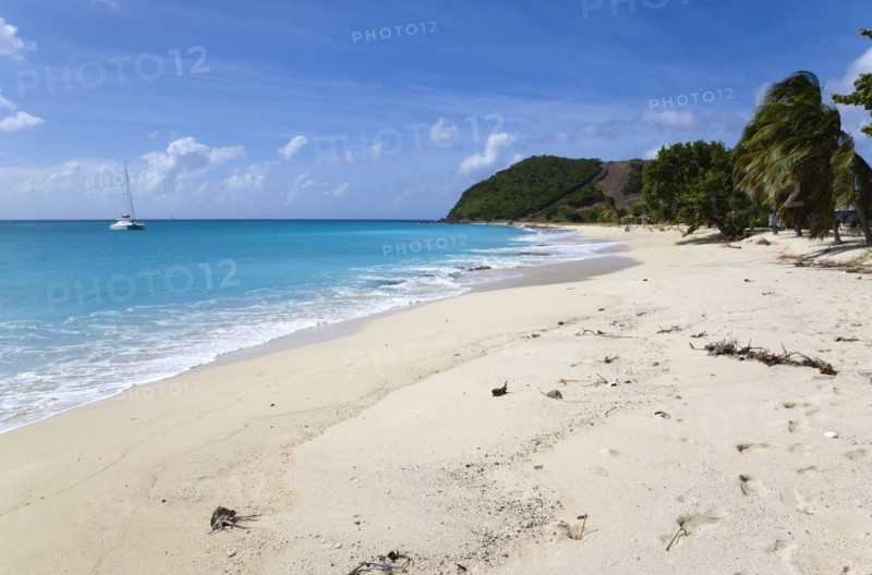 WEST INDIES, St Vincent & The Grenadines, Canouan, South Glossy Beach in Glossy bay with waves from the turqoise sea breaking on the shore and a yacht at anchor in the bay.