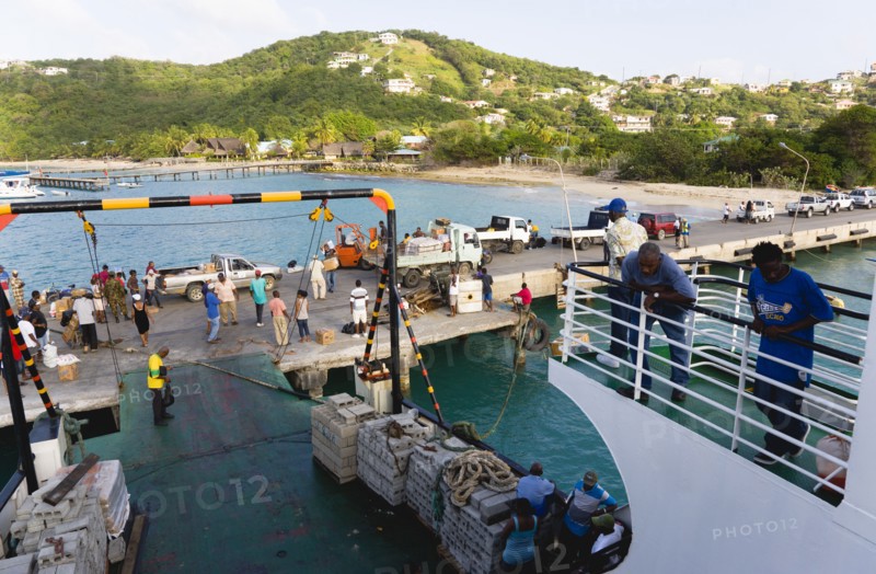 WEST INDIES, St Vincent & The Grenadines, Canouan, Charlestown Bay Inter island ferry at jetty with people walking amongst trucks with cargo unloaded from boat.
