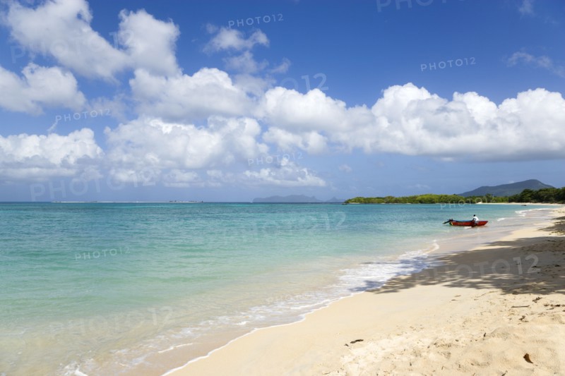 WEST INDIES, Grenada, Carriacou, Waves breaking on Paradise Beach at L'Esterre Bay with a fisherman beaching his boat and the turqoise sea and Sandy Island sand bar beyond.