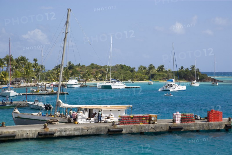 WEST INDIES, St Vincent & The Grenadines, Union Island, Inter island supply boat unloading provisions onto the main jetty in Clifton with yachts behind moored by the Anchorage Yacht Club in Clifton Harbour.