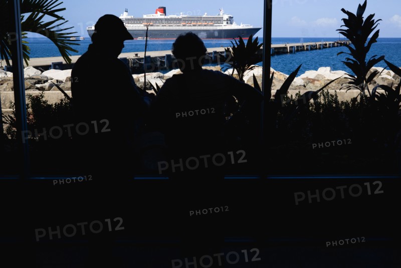 WEST INDIES, Grenada, St Georges, Tourists in the Cruise Ship Terminal looking out through the glass window towards the Queen Mary 2 liner moored offshore.