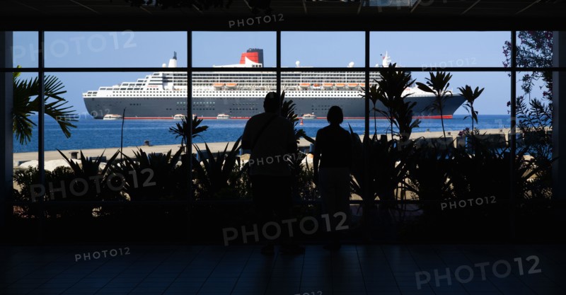 WEST INDIES, Grenada, St Georges, Tourists in the Cruise Ship Terminal looking out through the glass window towards the Queen Mary 2 liner moored offshore.