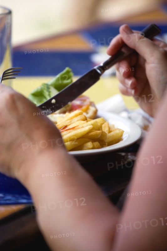 WEST INDIES, Grenada, St George, Sunburnt white caucasian woman eating a plate of potato chips and tomato ketchup with a knofe and fork.