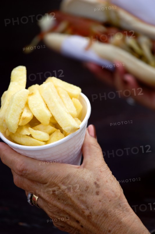 ENGLAND, West Sussex, Findon, Findon village Sheep Fair Elderly lady holding a polystyrene mug full of potato fries in one hand and a hot dog with tomato ketchup and onions in the other.