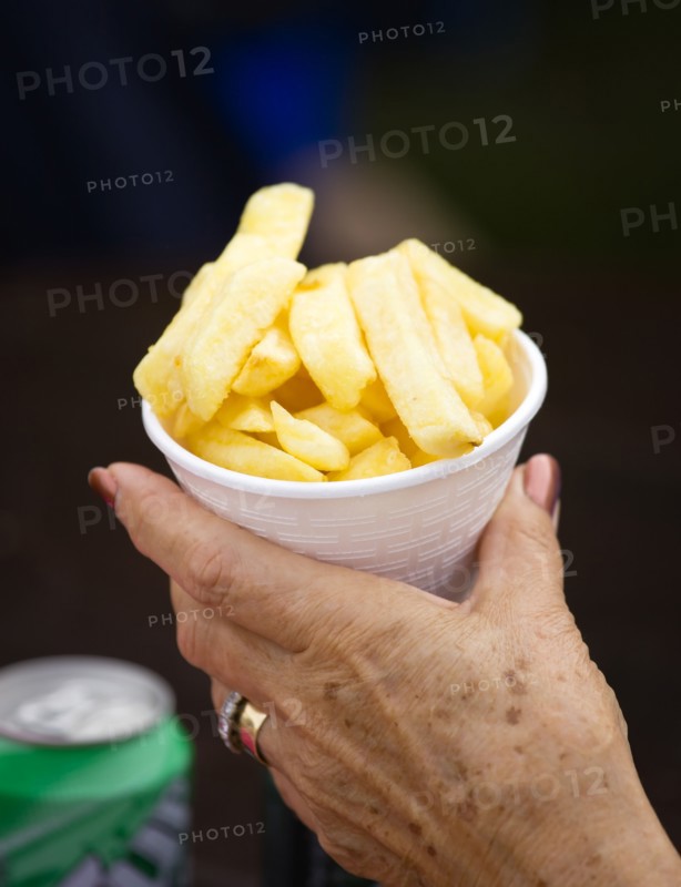 ENGLAND, West Sussex, Findon, Findon village Sheep Fair Elderly lady holding a polystyrene mug full of potato fries in one hand.