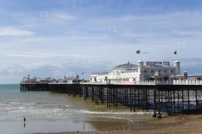 ENGLAND, East Sussex, Brighton, The Pier at low tide with a woman walking towards the water.