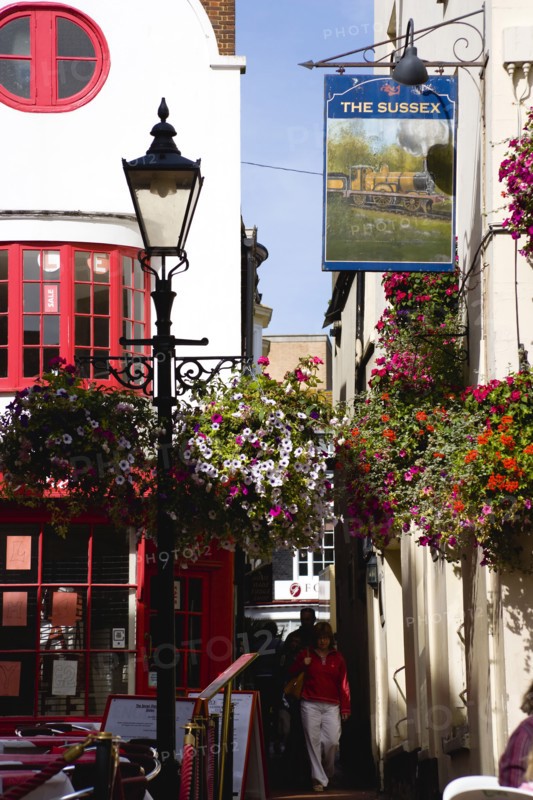 ENGLAND, East Sussex, Brighton, The Lanes Old fashioned streetlight lamppost outside The Sussex Pub with flowers in window boxes and hanging baskets and people walking in the narrow alley.