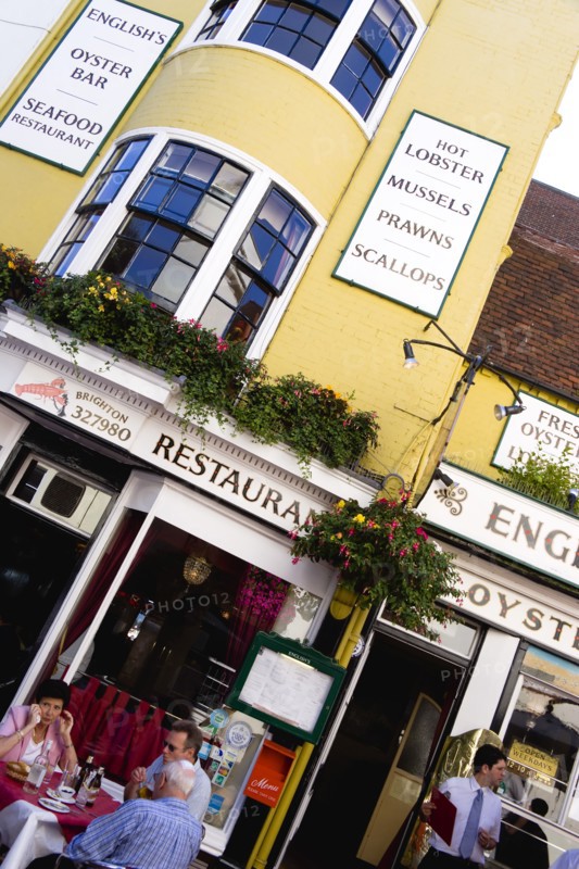 ENGLAND, East Sussex, Brighton, The Lanes Englishs Oyster Bar and Seafood Restaurant exterior with people sitting at a table eating lunch and a waiter by the entrance.