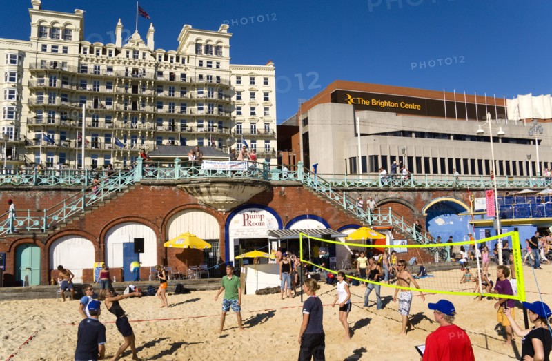 ENGLAND, East Sussex, Brighton, Young people playing beach volleyball on sand on the seafront with the De Vere Grand Hotel and The Brighton Centre beyond.