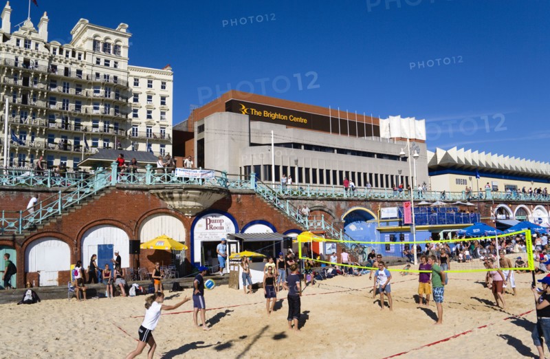 ENGLAND, East Sussex, Brighton, Young people playing beach volleyball on sand on the seafront with the De Vere Grand Hotel and The Brighton Centre beyond.