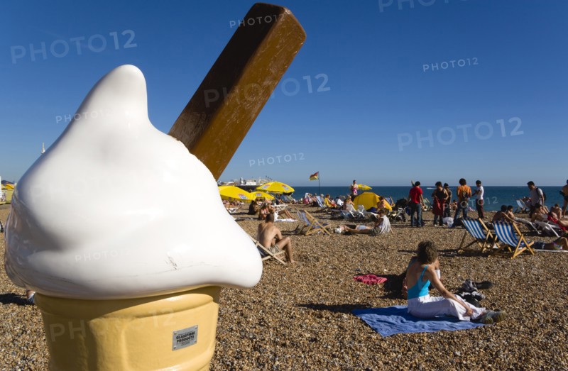 ENGLAND, East Sussex, Brighton, People sunbathing on the pebble shingle beach with a giant fibreglass model of an ice cream cone in the foreground.