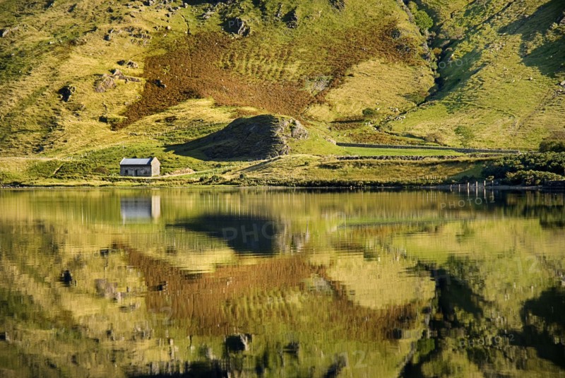 IRELAND, County Galway, Connemara, Kylemore Lough with reflection of stone cottage and animal like shape on hillside.