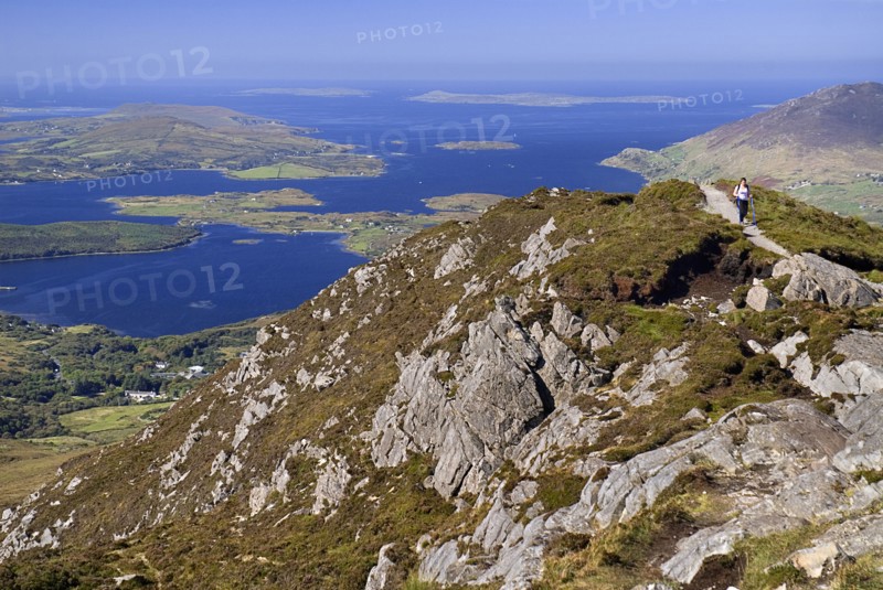 IRELAND, County Galway, Connemara, Diamond Hill, A hiker approaches the summit with Ballynakill Harbour in the background.