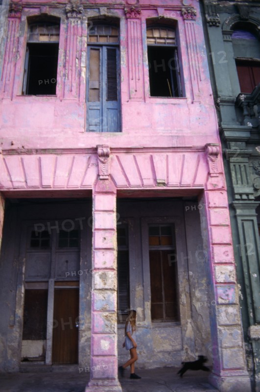 CUBA, Havana, Pink painted crumbling facade of house on the Malecon with girl and dog walking past.