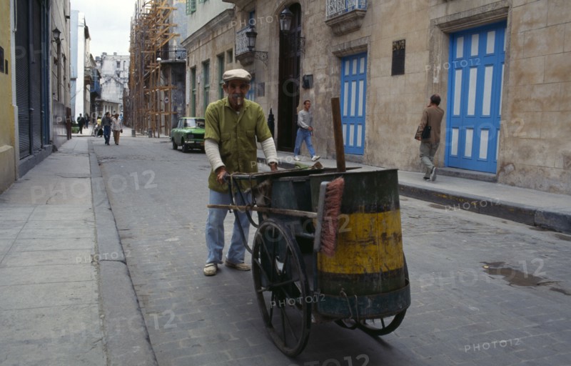 CUBA, Havana, Street cleaner pushing hand cart and smoking cigar.